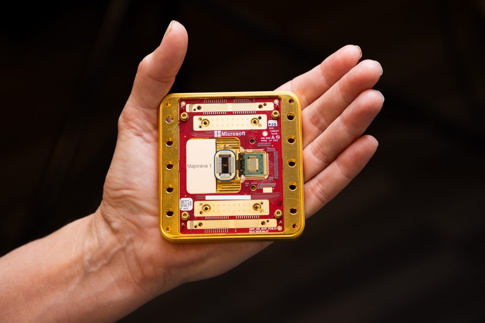 A large, gold-framed Majorana 1 chip is held by a human hand